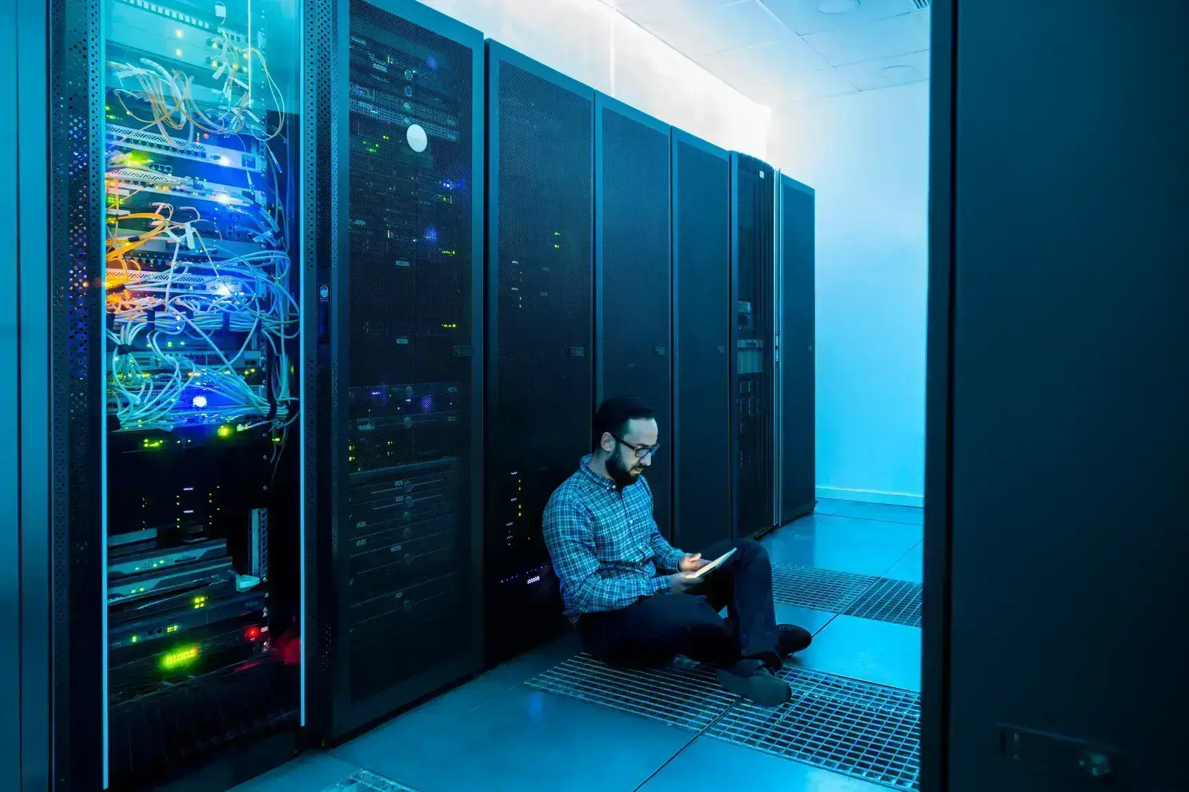 A man sits on the floor of a server room with his tablet