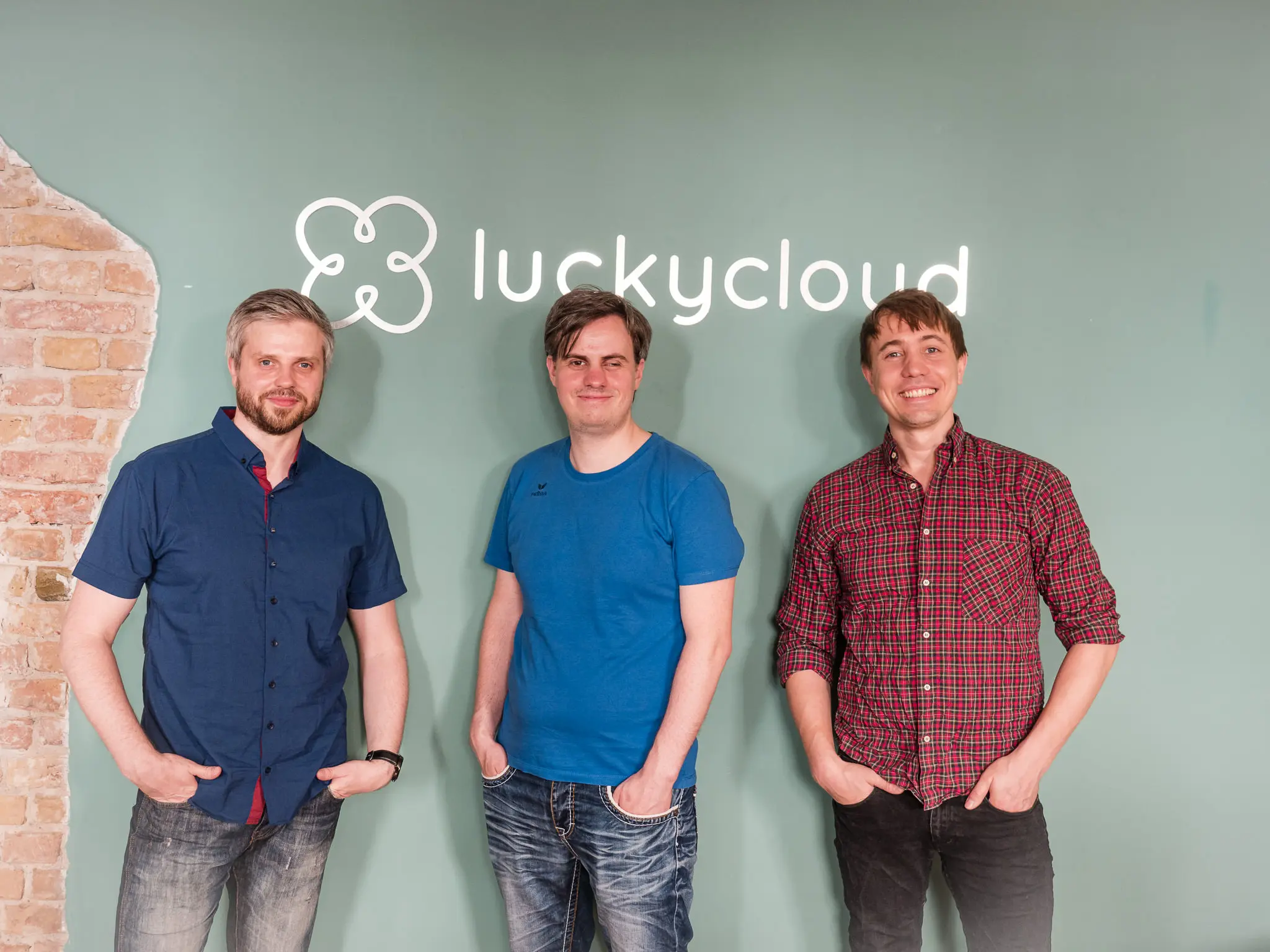 Drei luckycloud-Mitarbeiter positionieren sich vor dem Firmenschriftzug.