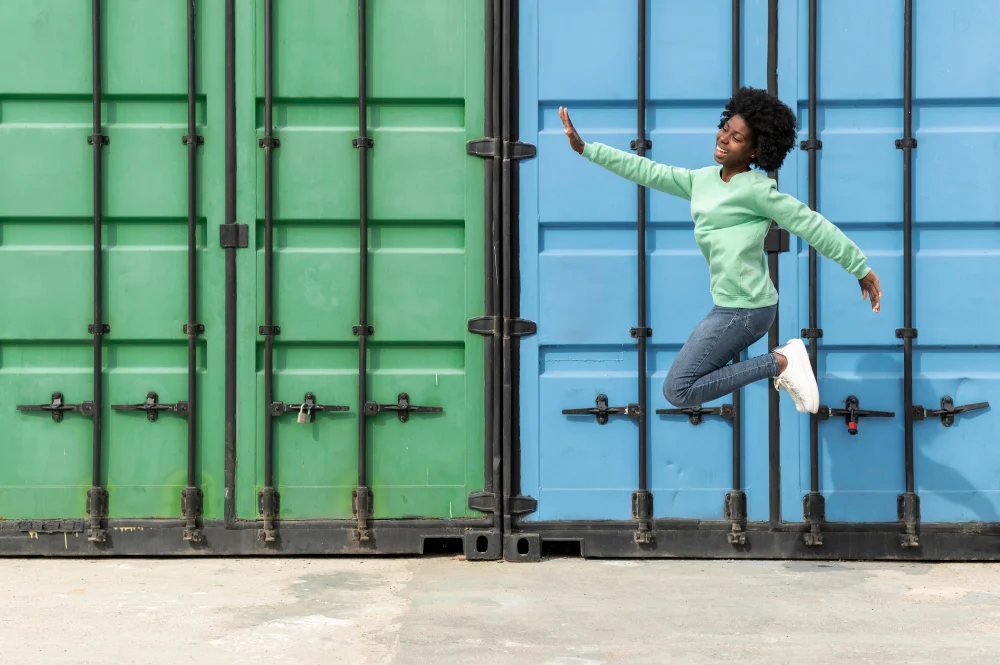 Bild einer jungen Frau, die vor einem grünen und einem blauen Container in die Luft springt