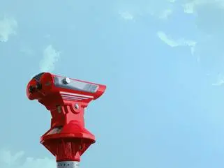 Ein rotes Standfernglas steht vor einem blauen Himmel.