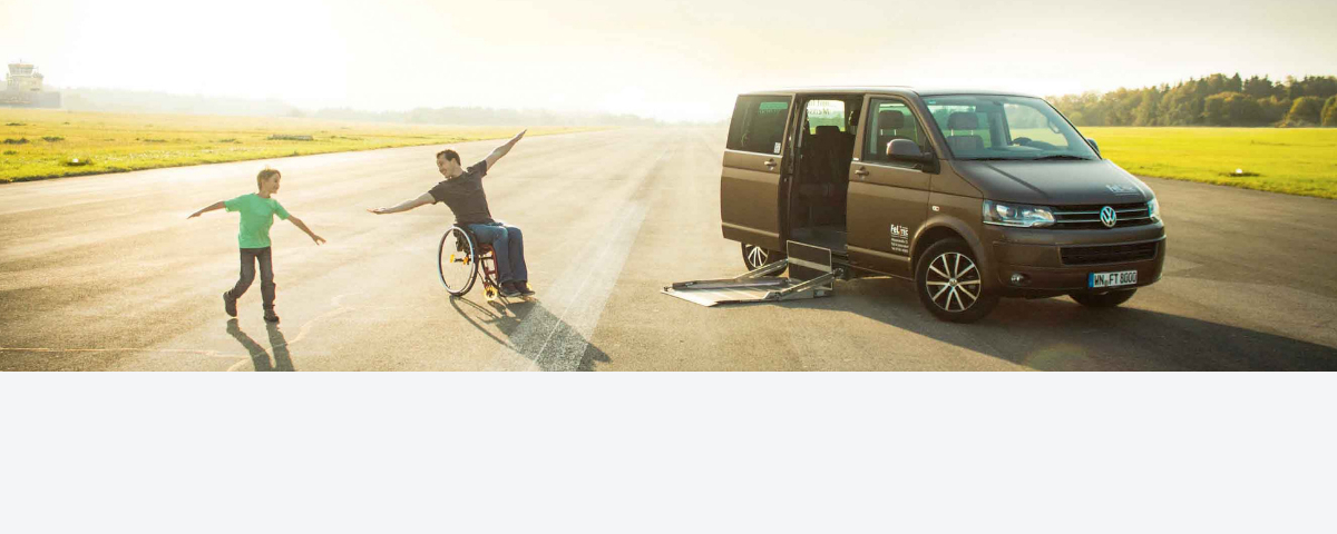 A man in a wheelchair romps with his son in front of a vehicle that has been modified to accommodate the disabled.
